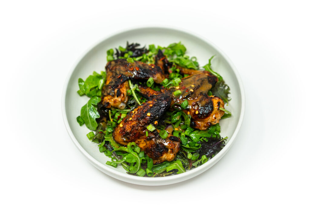 Whole grilled chicken wings glazed with citrus brown sugar mojo sauce, garnished with herbs and green onions on a dark plate