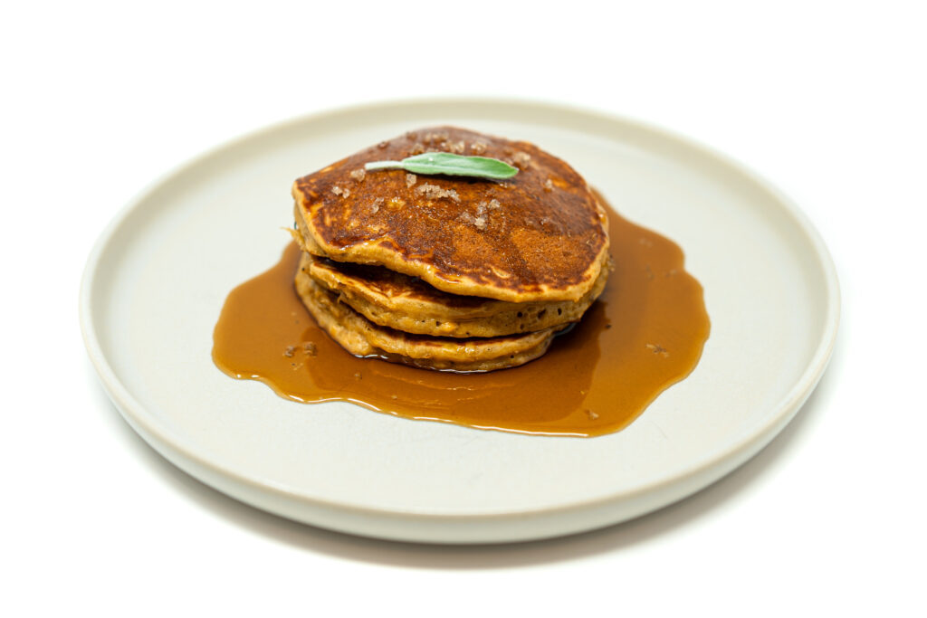 Stack of golden plantain pancakes drizzled with coffee liqueur syrup on a white plate.