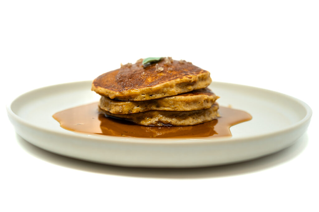 Stack of golden plantain pancakes drizzled with coffee liqueur syrup on a white plate.