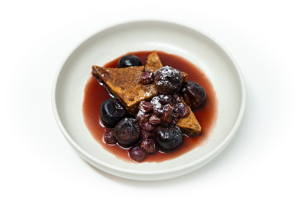 A plate of almond butter blondies topped with poached figs and grapes in red wine vanilla syrup, finished with powdered sugar and vanilla salt.