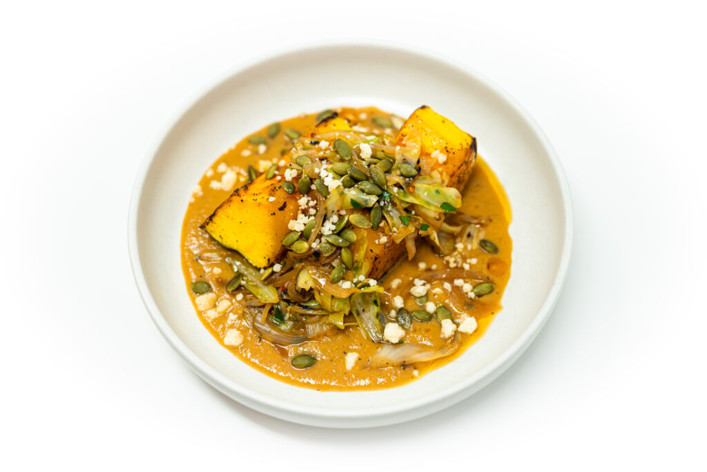 Seared pumpkin steak with miso brown butter sauce, charred cabbage, onion, chili oil, pepitas, and Parmesan on a plate