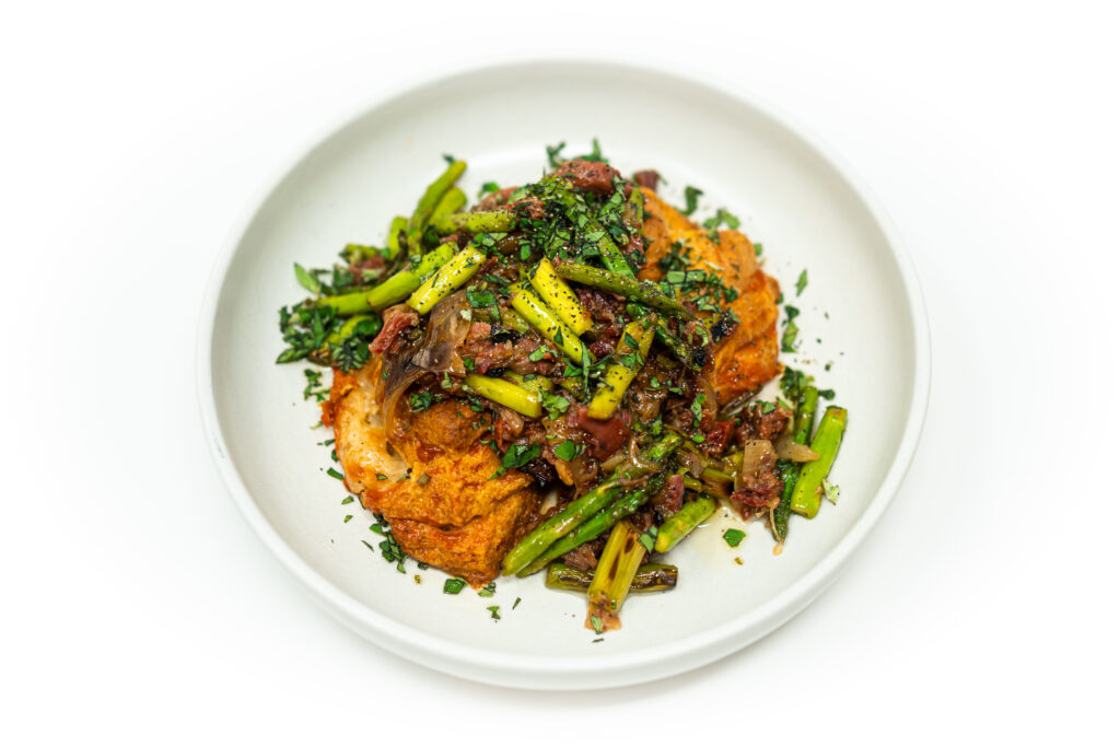 A plate of golden white cheddar biscuits topped with tender ham confit and charred asparagus, finished with fresh herbs.