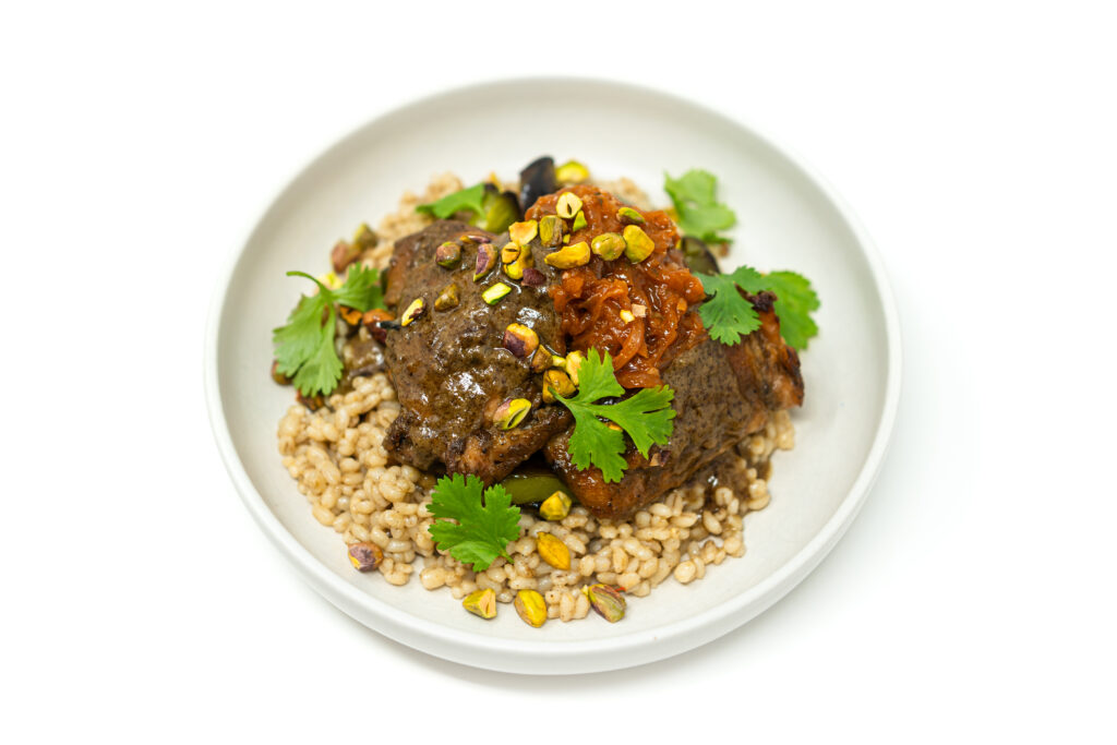 Chicken thighs simmering in a dark mole beer braising sauce with dried chiles, onion, and aromatics.