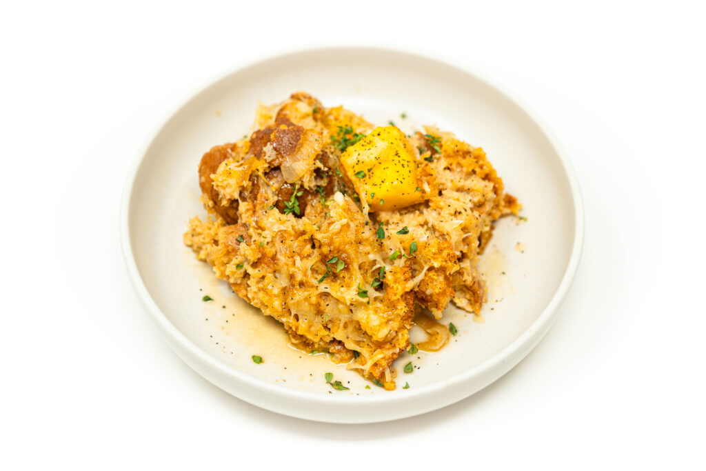 A serving of pumpkin and caramelized onion ciabatta bread pudding topped with herbs on a white plate.