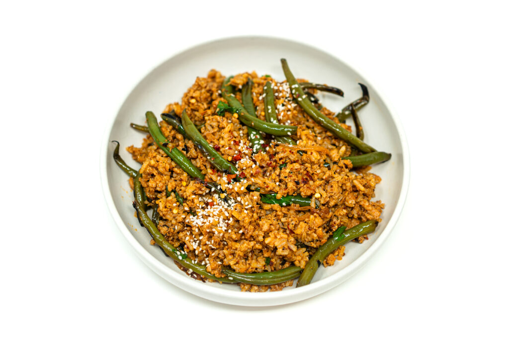 Wok filled with ground chicken stir fry tossed with charred green beans and rice.