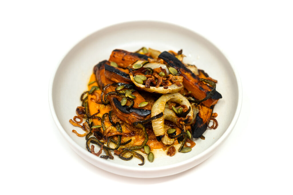 Charred sweet potato and fennel confit in olive oil served with herbs on a rustic plate.