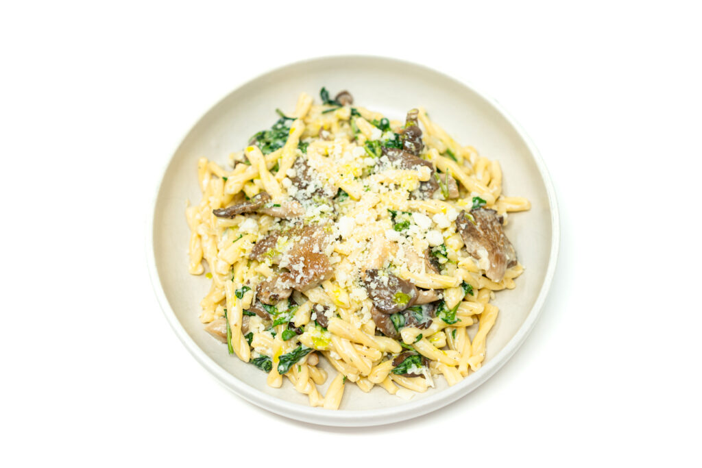 Creamy garlic trofie pasta with oyster mushrooms, arugula, and lemon zest served in a white bowl.
