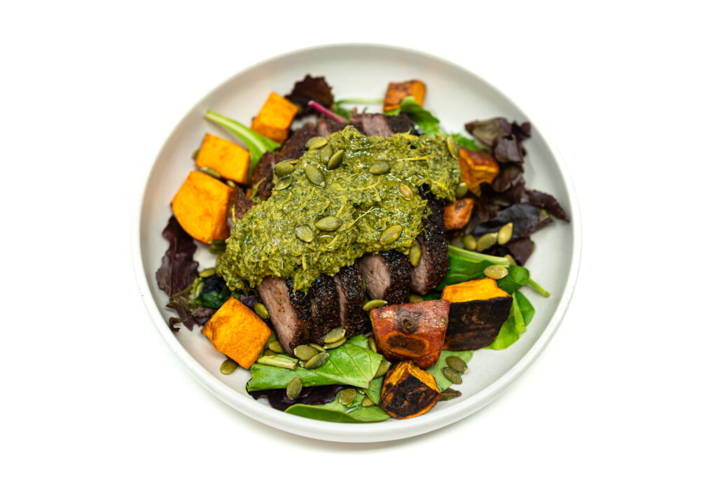 Sliced reverse seared tri tip steak topped with callaloo herb salsa served over roasted sweet potatoes and mixed greens.