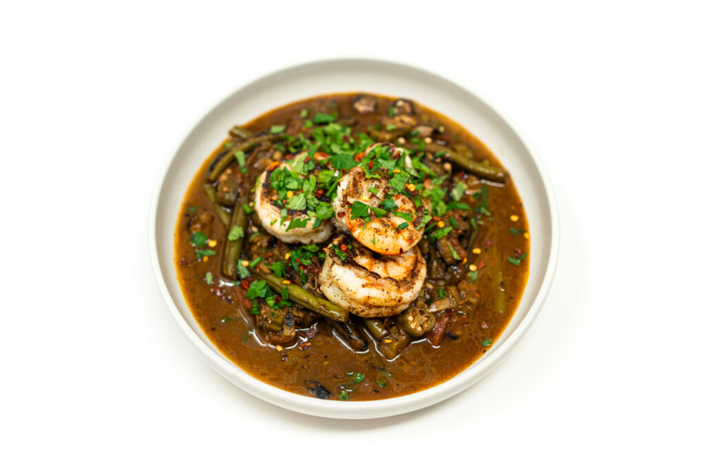 Plate of Jordanian style spiced vegetable stew with green beans and okra topped with lemon butter seared shrimp and fresh herbs.