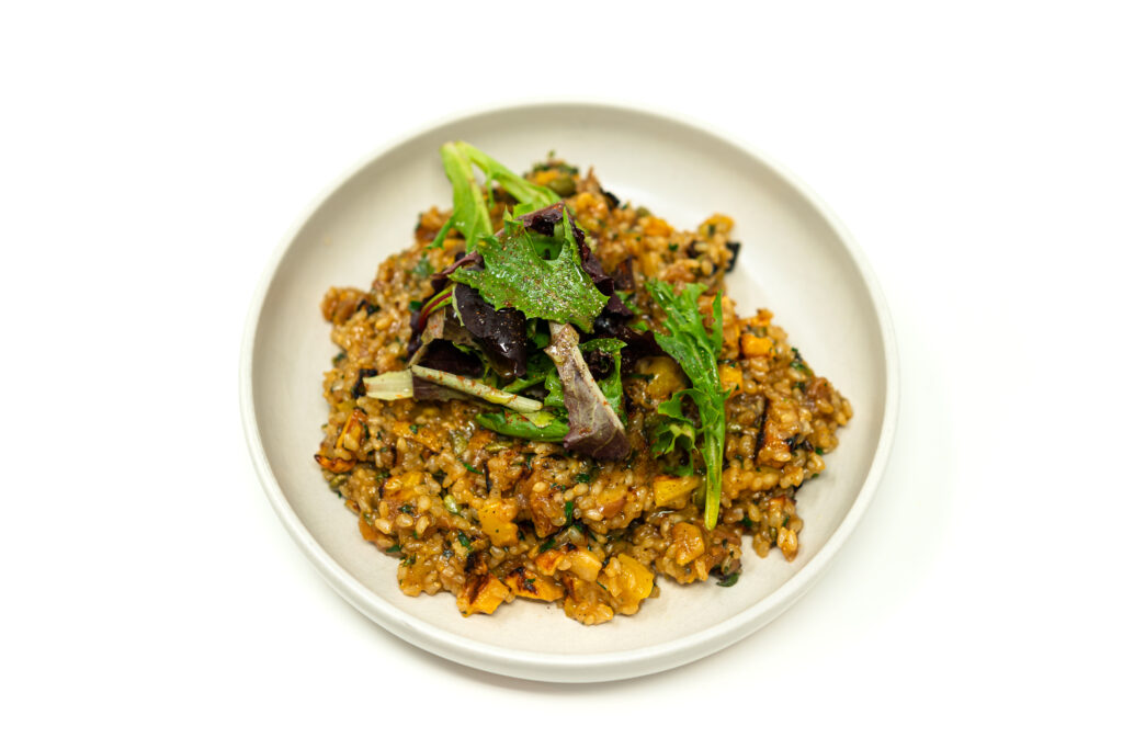 Top-down view of a white ceramic bowl filled with sweet brown rice pilaf and roasted delicata squash, topped with a fresh salad of mixed greens.