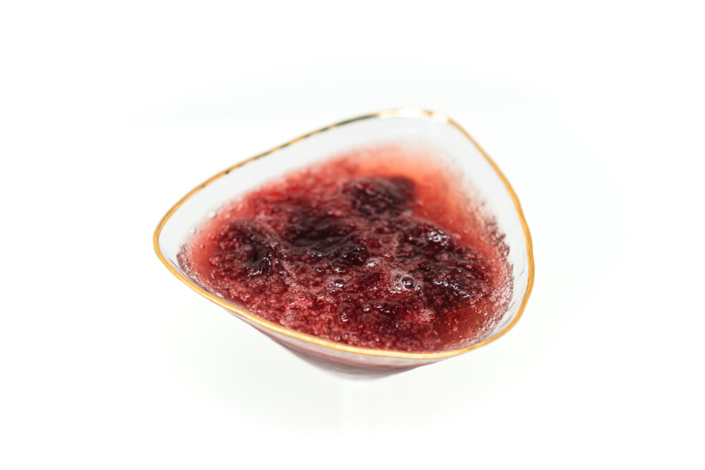Overhead shot of a crystal coupe glass filled with dark red frozen gamay wine granita topped with bubbles and champagne, set against a stark white background.