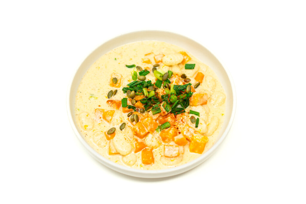 A white bowl filled with garlic cheese curd gnocchi, roasted butternut squash, and cream sauce topped with pepitas and green onions.
