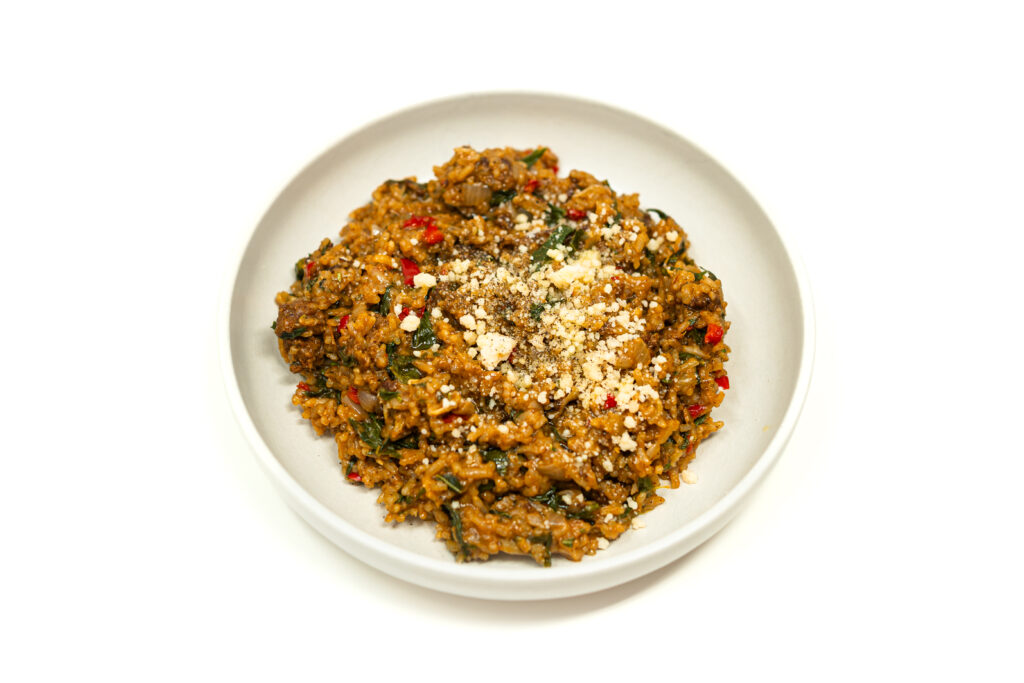 A plated serving of one pot chorizo and rice pilaf with wilted turnip greens, red peppers, and a garnish of Parmesan cheese in a white bowl.