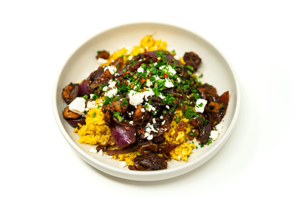 Bowl of sherry vinegar glazed chicken thighs and sautéed red onions served over yellow saffron rice garnished with crumbled feta cheese and chopped parsley.