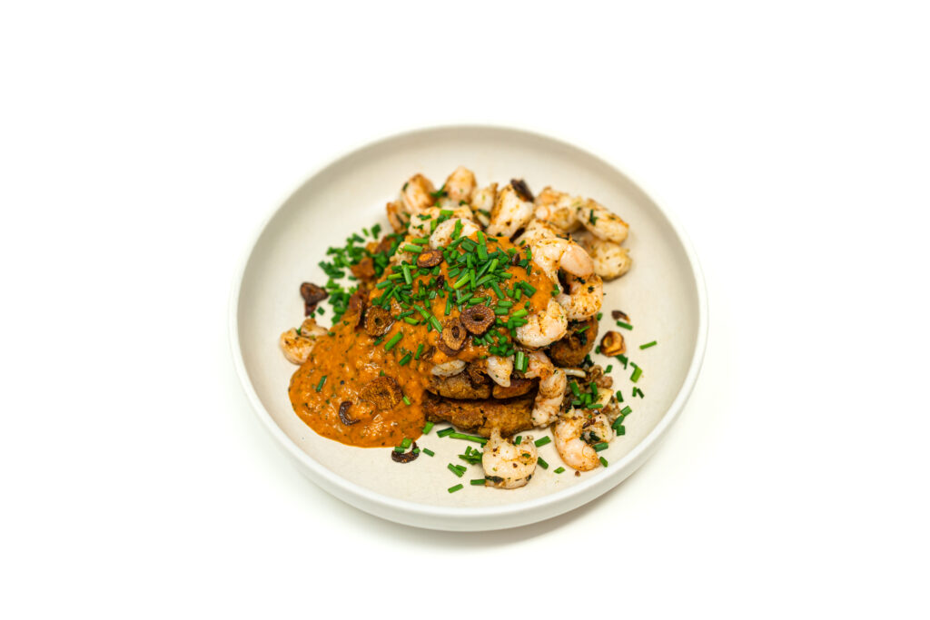 Crispy green banana mofongo patties topped with garlic chili shrimp and roasted tomato salsa on a white plate.