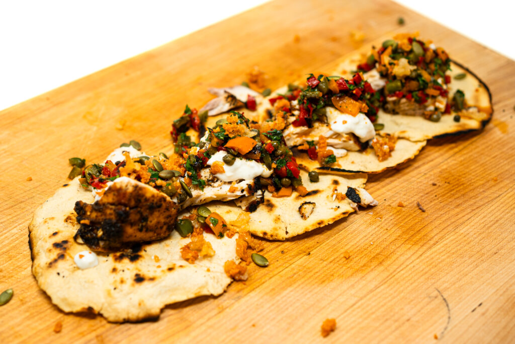 spiced amberjack tacos on charred corn tortillas, topped with fresh burrata cream, bright tri-color pepper relish, and crispy fried cheese shards.