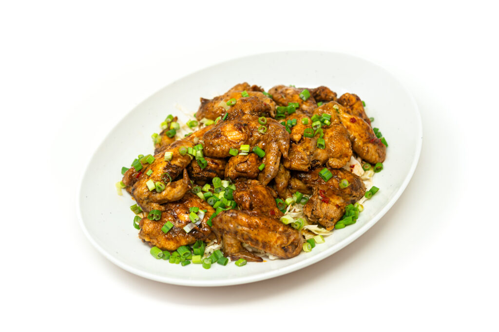 Close up of glossy braised buffalo wings plated next to a vibrant charred cabbage slaw.