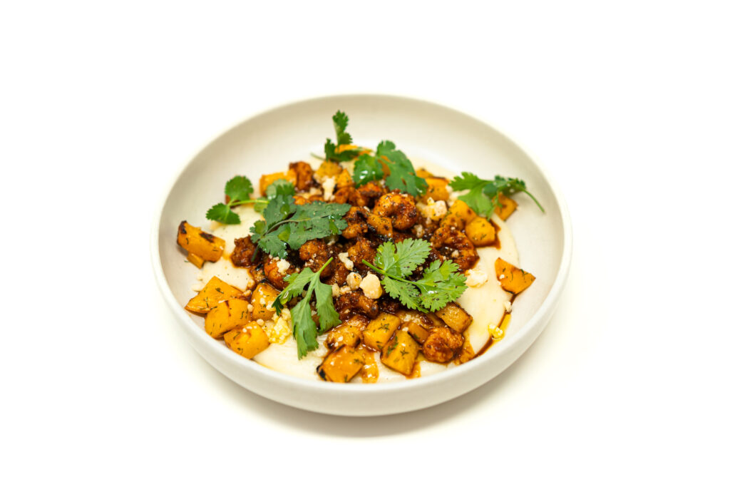 A shallow bowl of chili-lime rock shrimp served over creamy garlic whipped yuca and diced dill-roasted rutabaga, garnished with cilantro and cotija.
