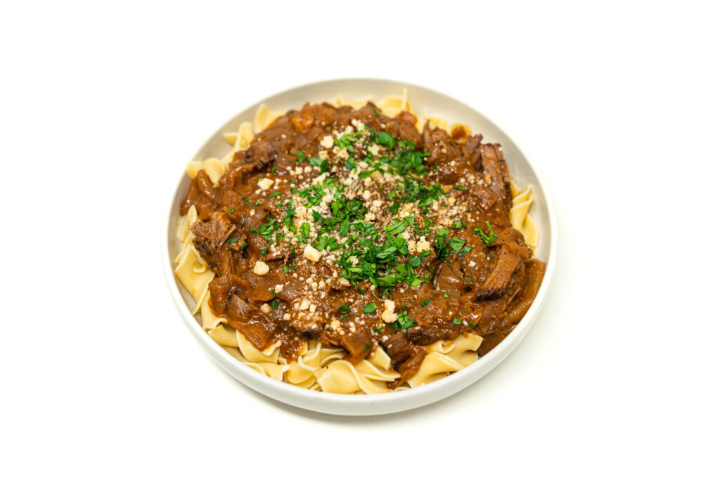 A rustic bowl of rich Beef Chuck Roast Goulash served over wide egg noodles and garnished with fresh parsley and grated Parmesan cheese.