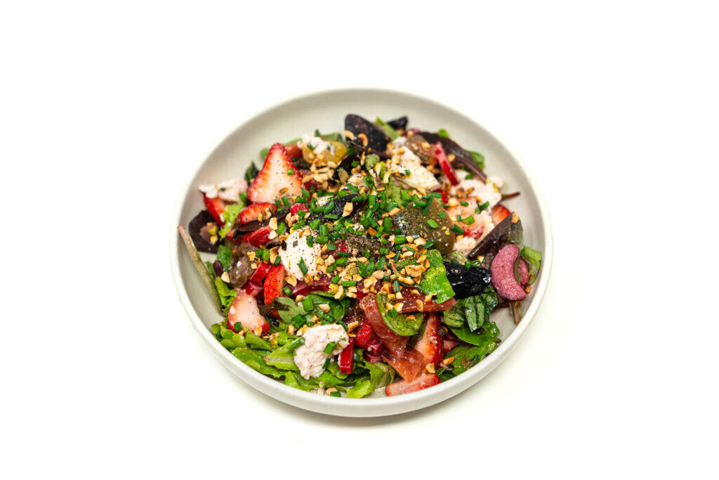 A shallow bowl filled with strawberry rhubarb caprese salad topped with fresh mozzarella, basil, and toasted hazelnuts.