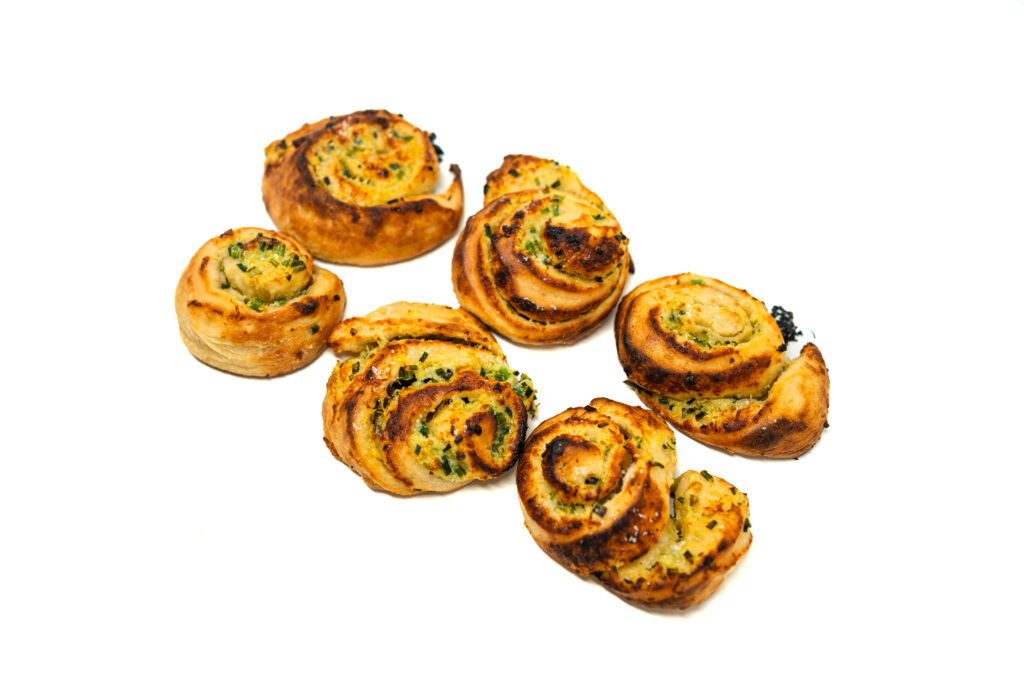 Six golden brown, blistered garlic chive pizza rolls sitting on a white background.