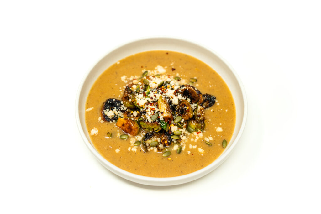 Top-down view of thick miso potato soup topped with blistered chili-garlic brussels sprouts and pepitas.