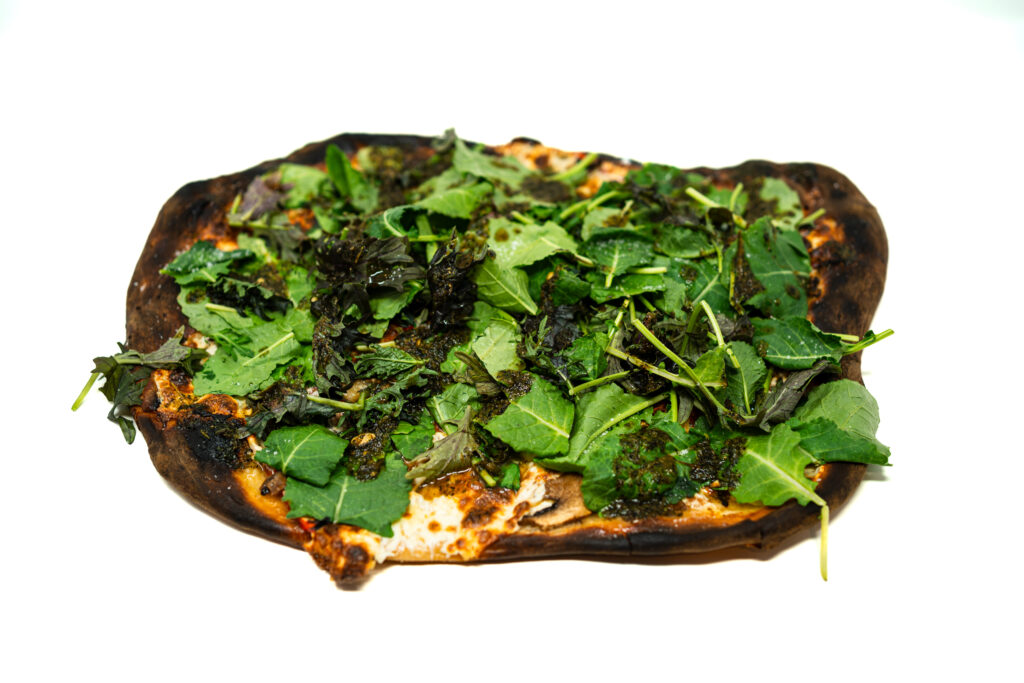 A blistering hot charred mozzarella pizza topped with fresh mixed greens and a vibrant green smoky serrano-citrus drizzle.