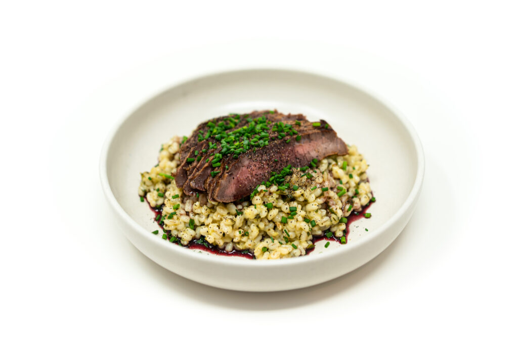 Sliced medium rare cast iron seared London broil over herb dijon barley with a pooled red wine reduction.
