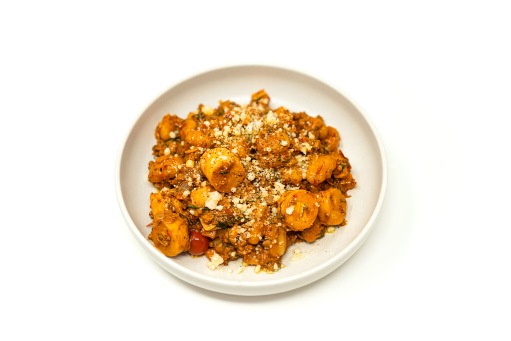 A white bowl filled with ground lamb and dill ragu, sliced hearts of palm, and soft gnocchi in a creamy tomato sauce.