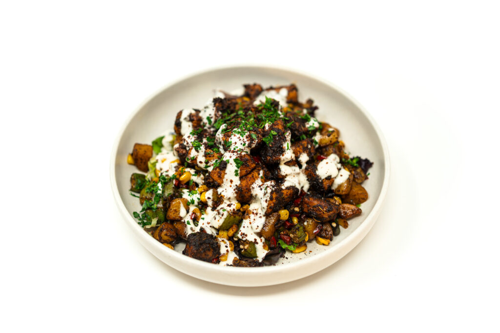 Plated Blackened Pork Bites resting on warm okra and corn succotash over mixed greens, drizzled with garlic aioli.