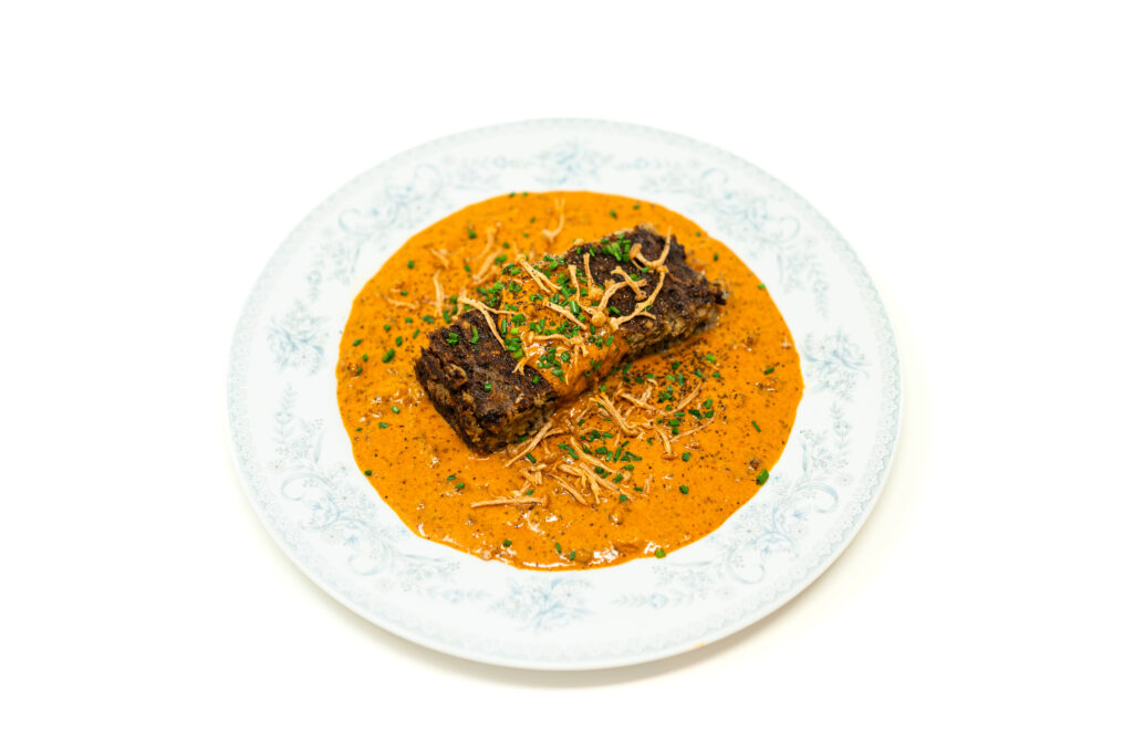 Thick slice of triple mushroom meatloaf resting in a pool of creamy chorizo onion sauce topped with crispy flash fried enoki mushrooms.