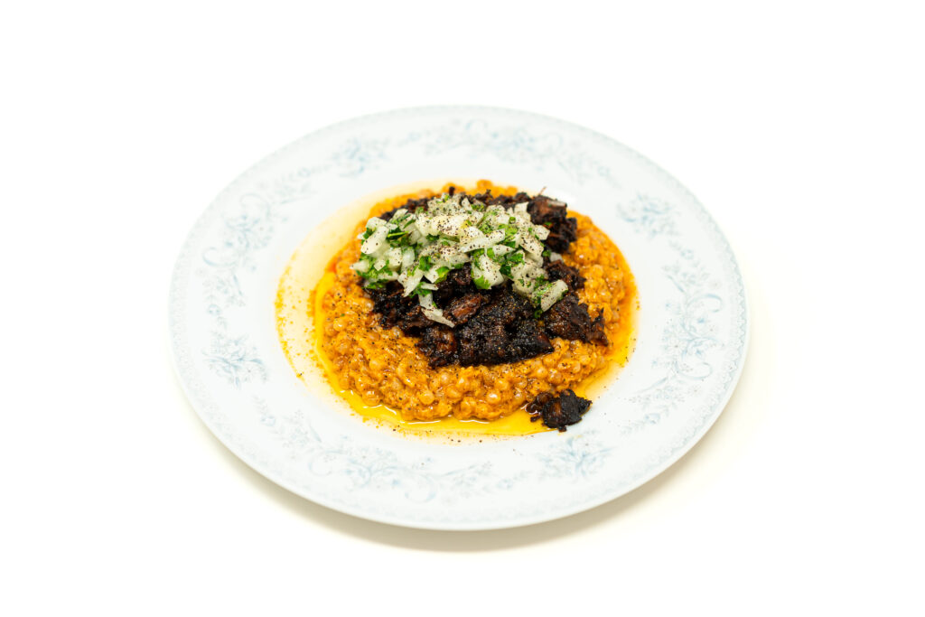 Crisped shredded oxtail served over sweet corn pearl couscous with a fresh onion and cilantro garnish.