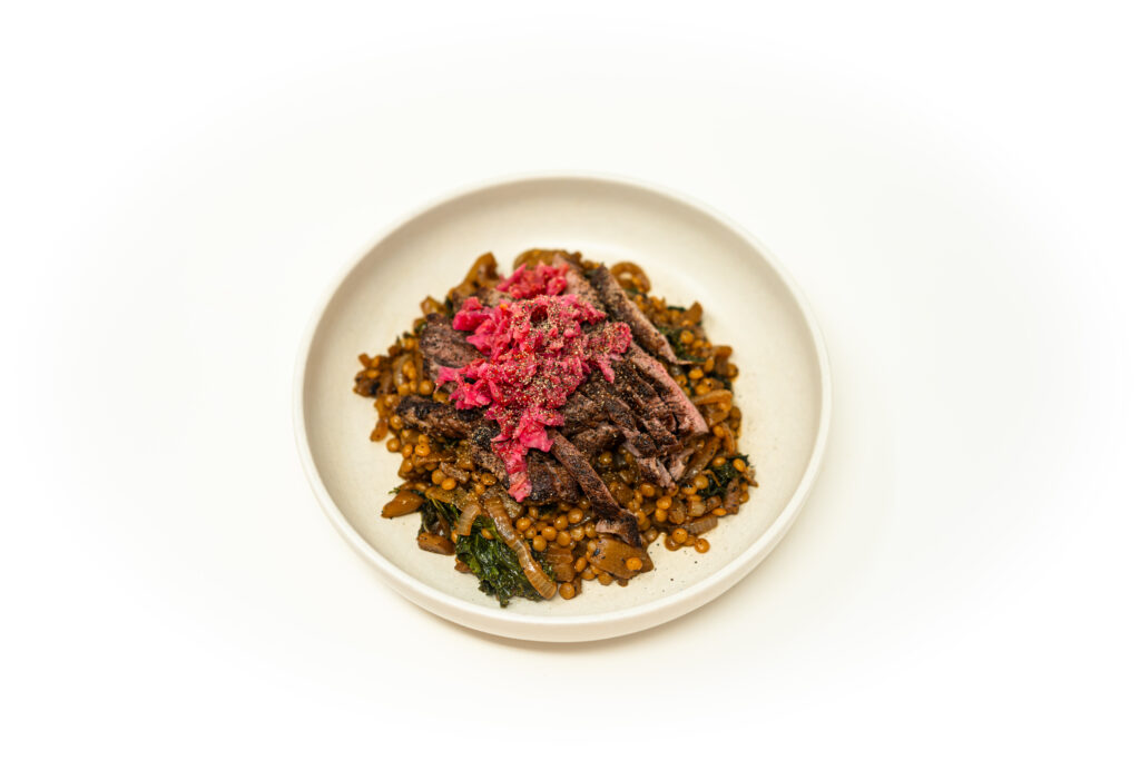 Sliced cast iron seared pork rib steak plated over braised chayote and kale pearl couscous.