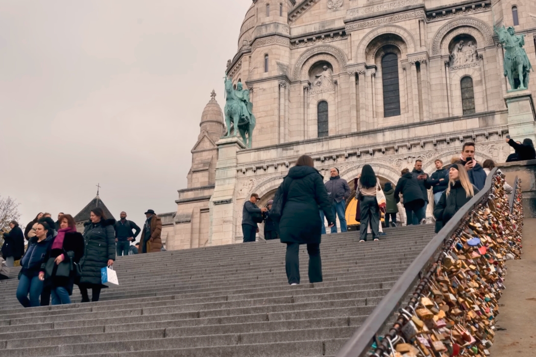 View of the Sacré-Cœur basilica dome in Montmartre, Paris, with pedestrians walking in the foreground.