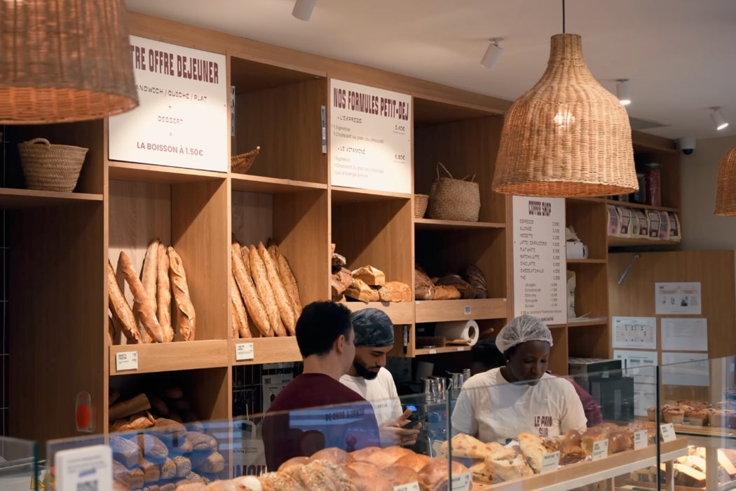 Interior of Tranche Bakery in Paris showing fresh bread on wooden shelves and a baker behind the counter.