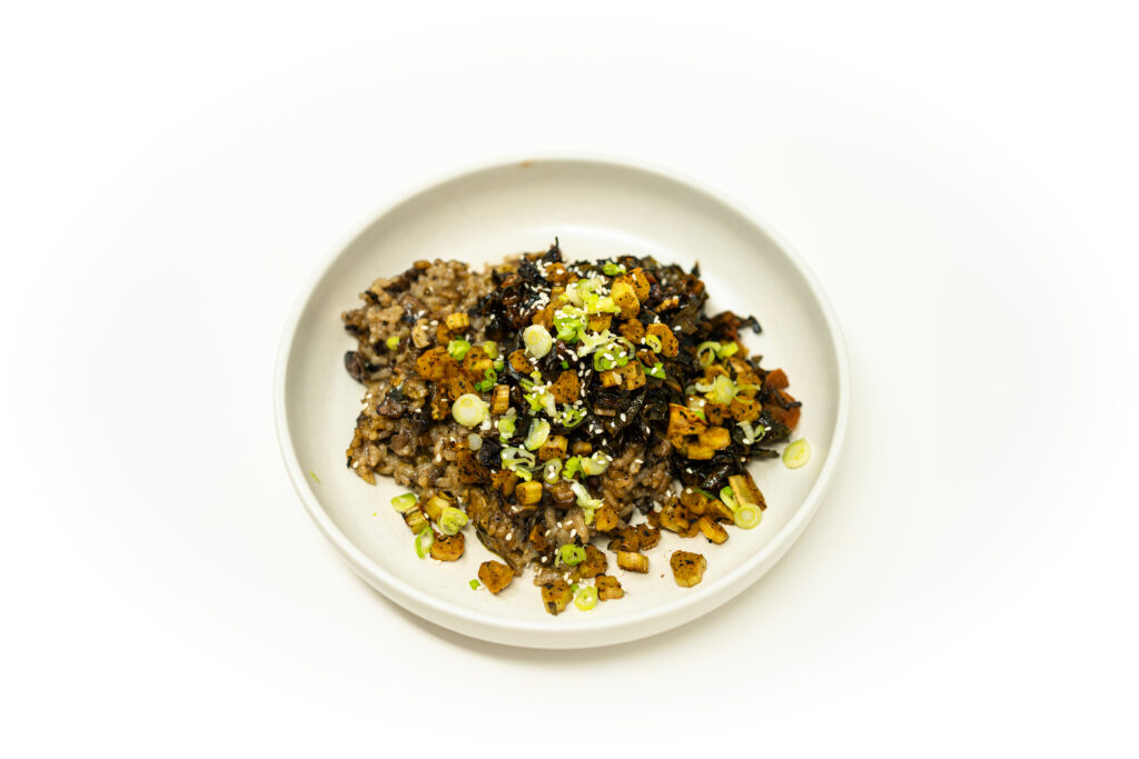 A cast iron skillet filled with crispy mushroom rice topped with gochujang braised collard greens and raw egg yolks.