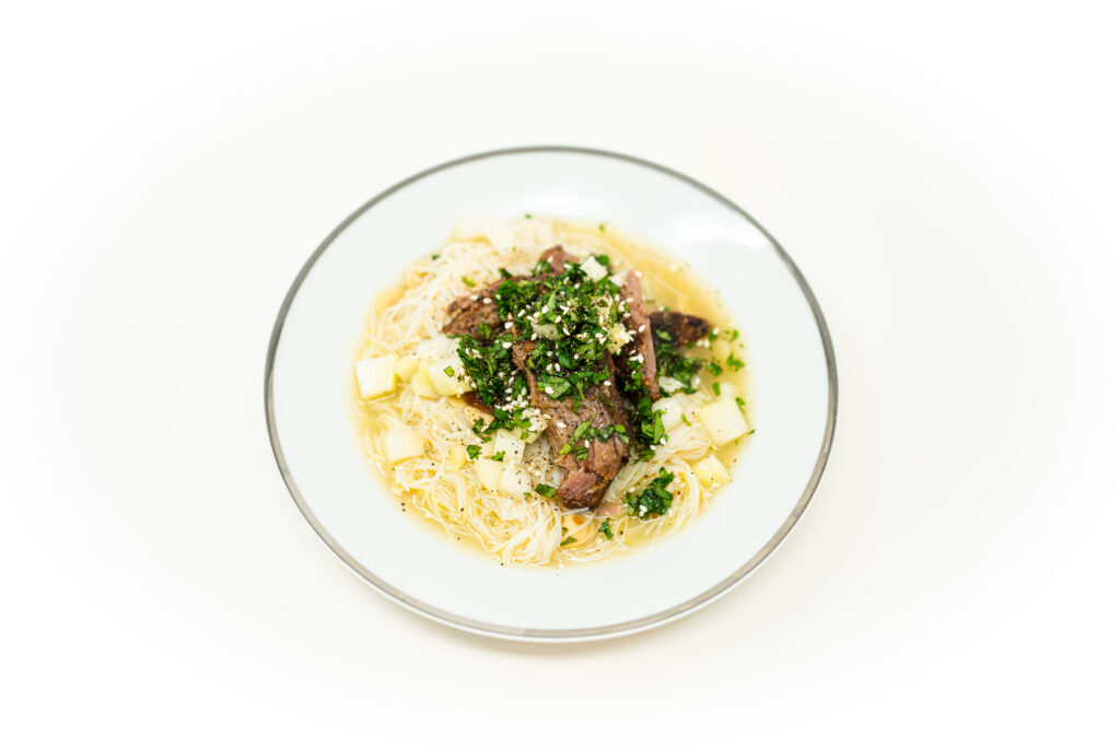 A shallow bowl of braised glass noodles topped with seared roast pork shoulder and diced pickled chayote.