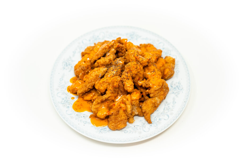 A plate of hot, crispy salt and vinegar brined chicken tenders smothered in a bright orange fermented chili emulsion, garnished with cracked black pepper.