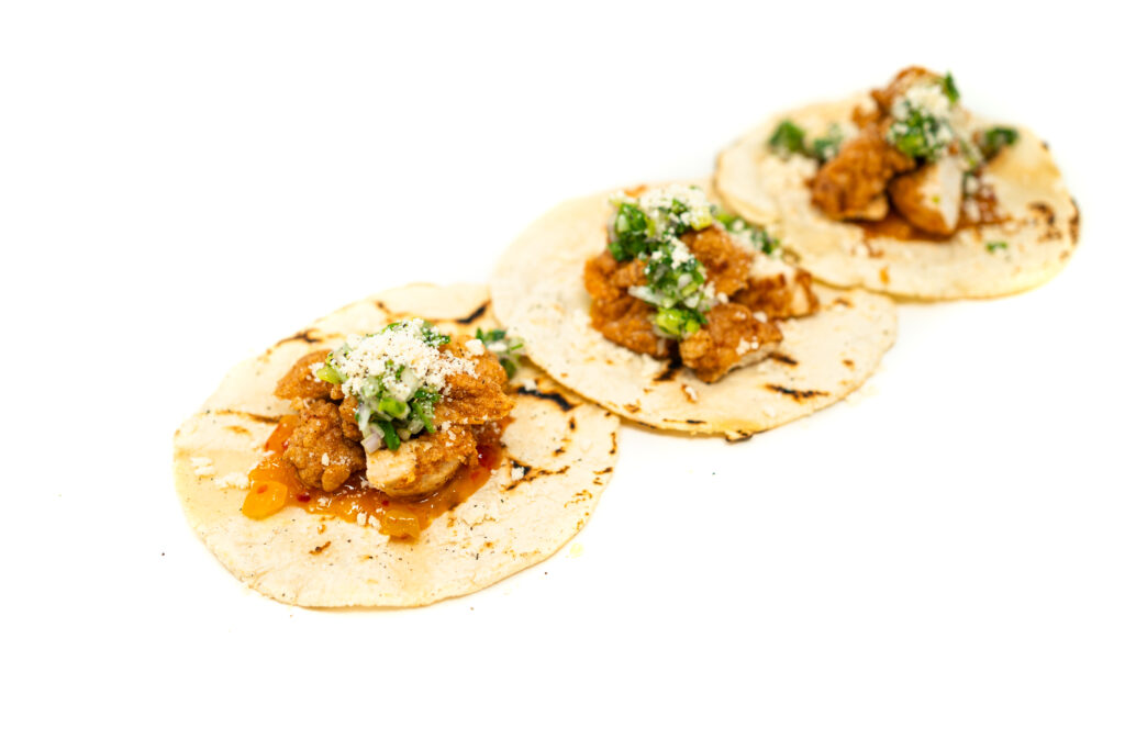 Three charred corn tortillas filled with crispy salt and vinegar fried chicken, sweet Vidalia relish, green onion salsa, and crumbled cotija cheese.