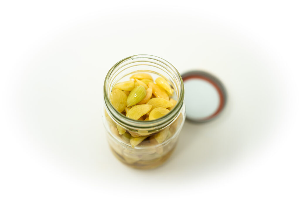 A clear glass jar filled with peeled garlic cloves submerged in a cloudy salt brine, demonstrating the lacto fermentation process.