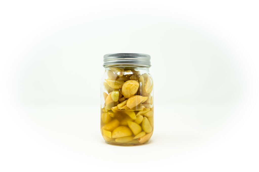 A clear glass jar filled with peeled garlic cloves submerged in a cloudy salt brine, demonstrating the lacto fermentation process.