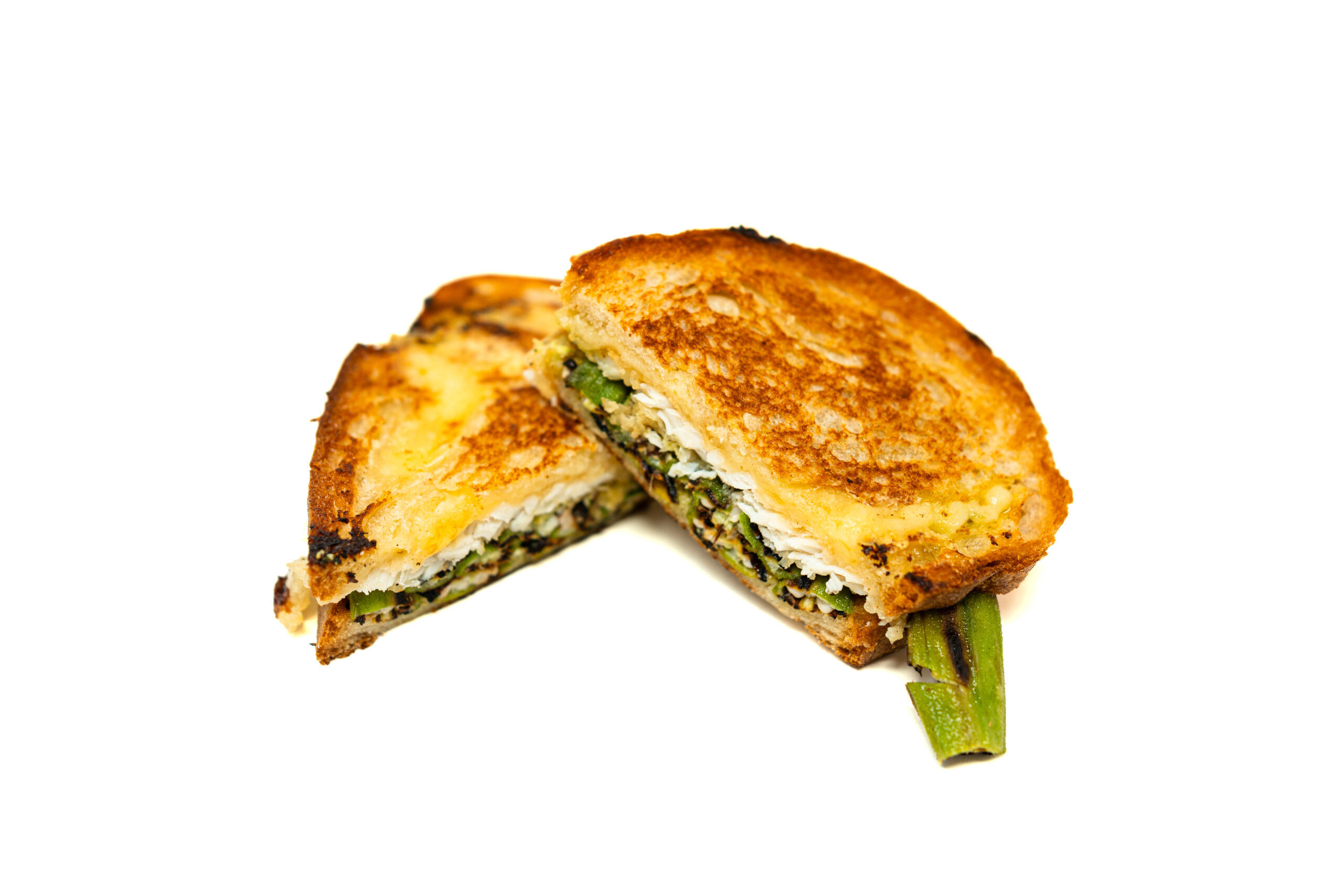 Cross-section of a fried triggerfish sandwich on a stainless prep table, showing melted Gruyère, a jagged cornmeal crust, and blistered okra under harsh overhead kitchen lighting.
