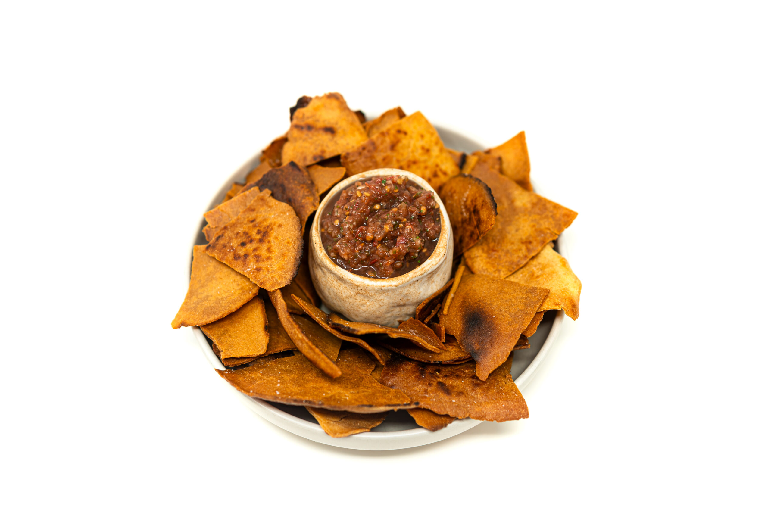 Overhead view of a stainless steel prep table featuring a bowl of thick fermented heirloom tomato salsa surrounded by blistered, golden masa chips fried in corn oil.