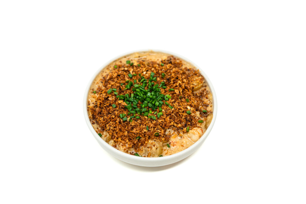 Overhead view of cooked rock shrimp and sliced potatoes coated in a glossy brown butter sauce, topped edge to edge with golden panko and green chives.