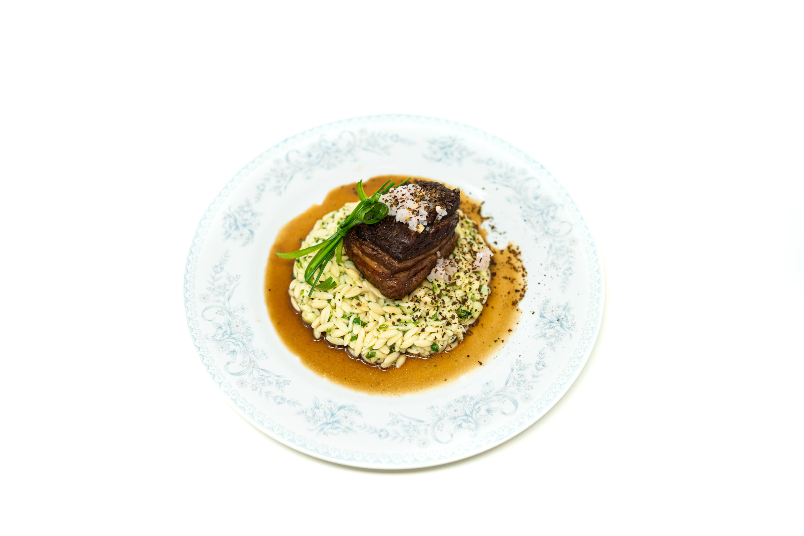 Square of broiled pork belly sitting on a bed of green-flecked orzo pasta, topped with pickled shallots and surrounded by a dark reduced kombu glaze.