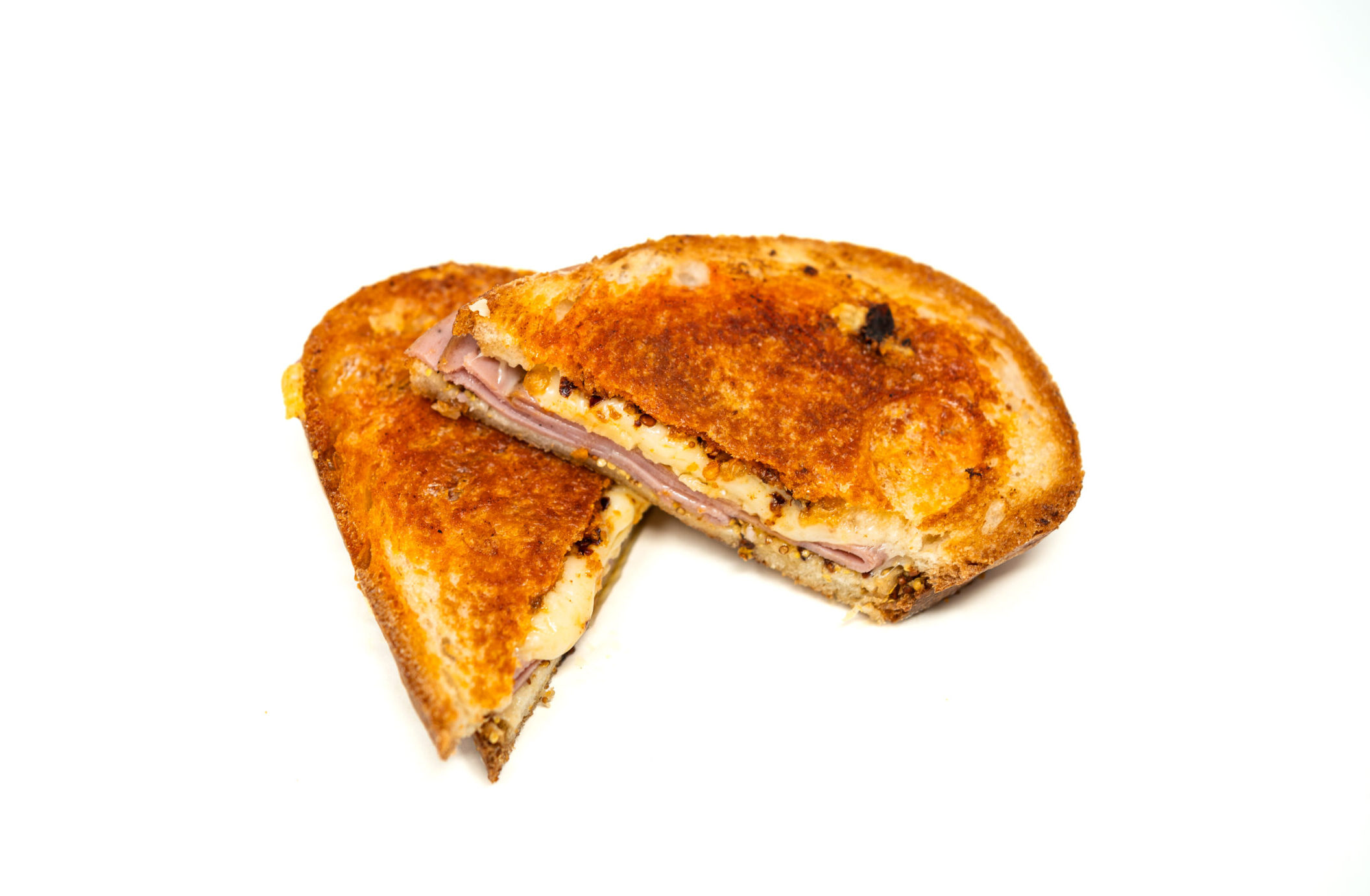 A halved pressed bologna sandwich resting on a bare metal prep surface. The cross-section reveals a thick slice of blistered meat, a layer of melted American cheese, and rigid fried shallots anchored in hot honey between two slices of deeply browned, mayo-toasted bread.